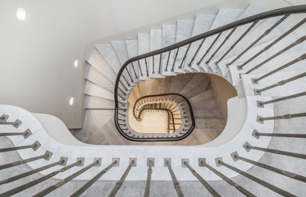 Winding cantilever stone staircase with patinated metal stair railing in a neutral colour scheme