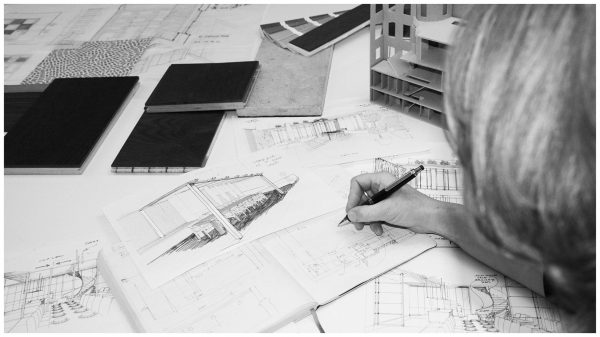 Female architect and interior designer working on hand-drawn sketches and detailed drawings, developing an interior design concept with the help of wood, stone and wallpaper samples