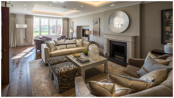 Living room in neutural tones with double coffer ceiling, white timber framed sash windows, stone fireplace, wood flooring and facing cream coloured sofas