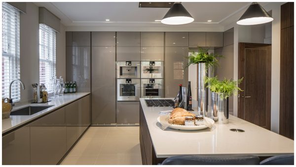 A clean-lined contemporary kitchen in a taupe colour with a large kitchen island with gas hob & recessed ceiling extractor, Gaggenau eyelevel ovens