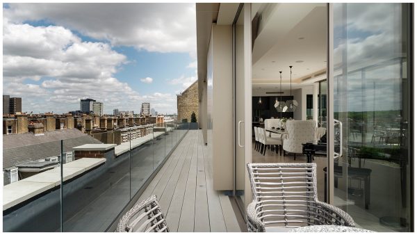 Wrap-around city balcony with views across rooftops and into the open plan living space, accessed through sliding glass doors from the outdoor seating area