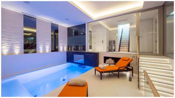 Basement swim spa, featuring tiled and mirrored walls, with relaxation area, overlooked by steam room and home cinema