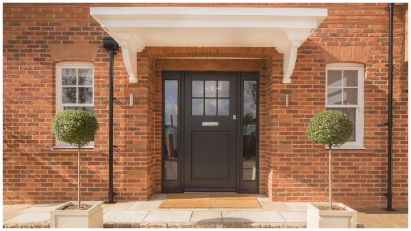Mottled red brick entrance portico with white porch canopy, creaser tile quoins & flat arch brickwork detail, matt black front door with glazed side-lights and flagstone pavers